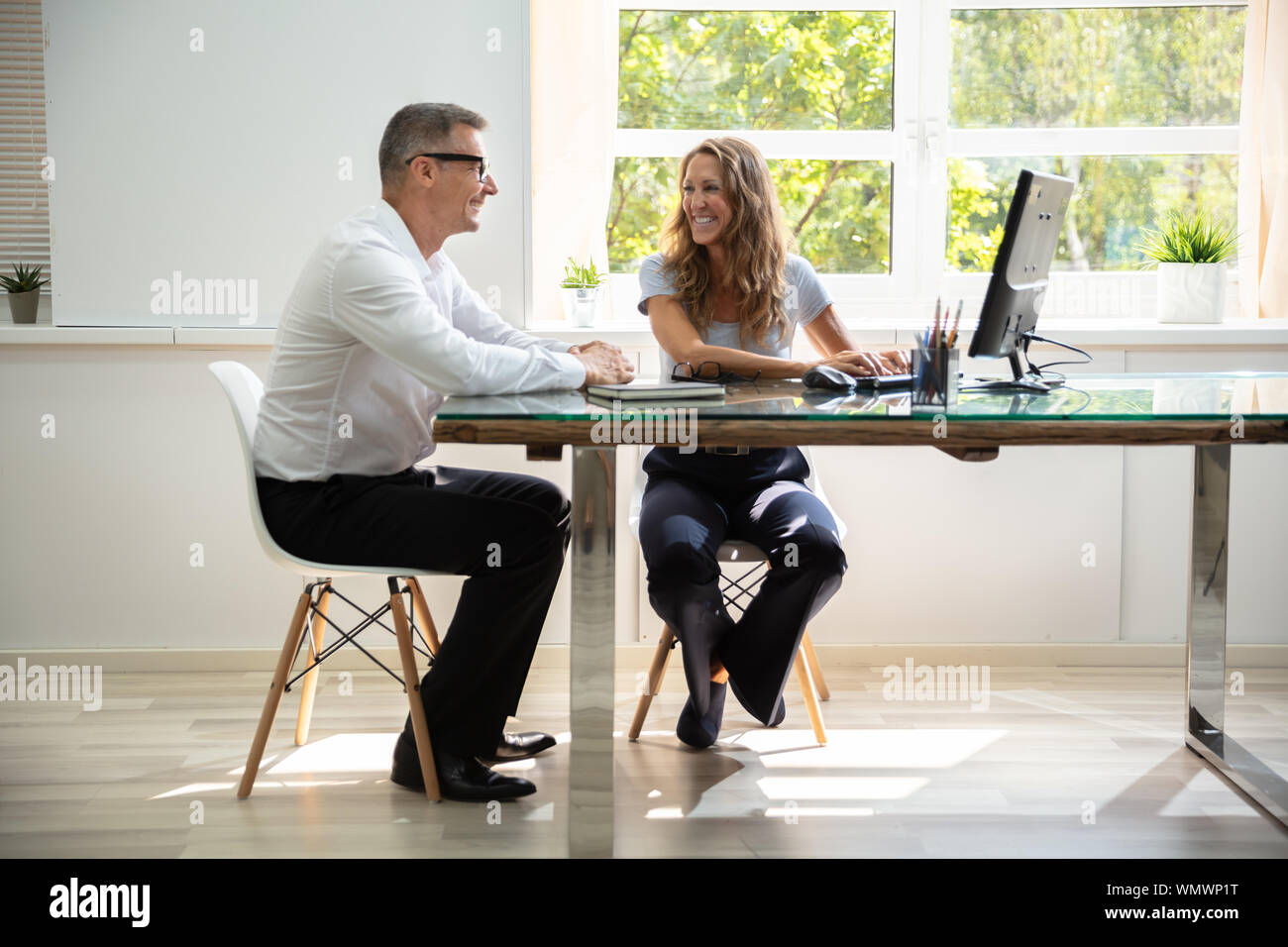 Smiling Male And Female Colleagues Sitting At Office Desk Working ...
