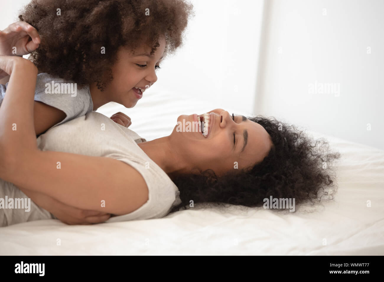 Happy black mother lying on bed, holding happy cute daughter. Stock Photo