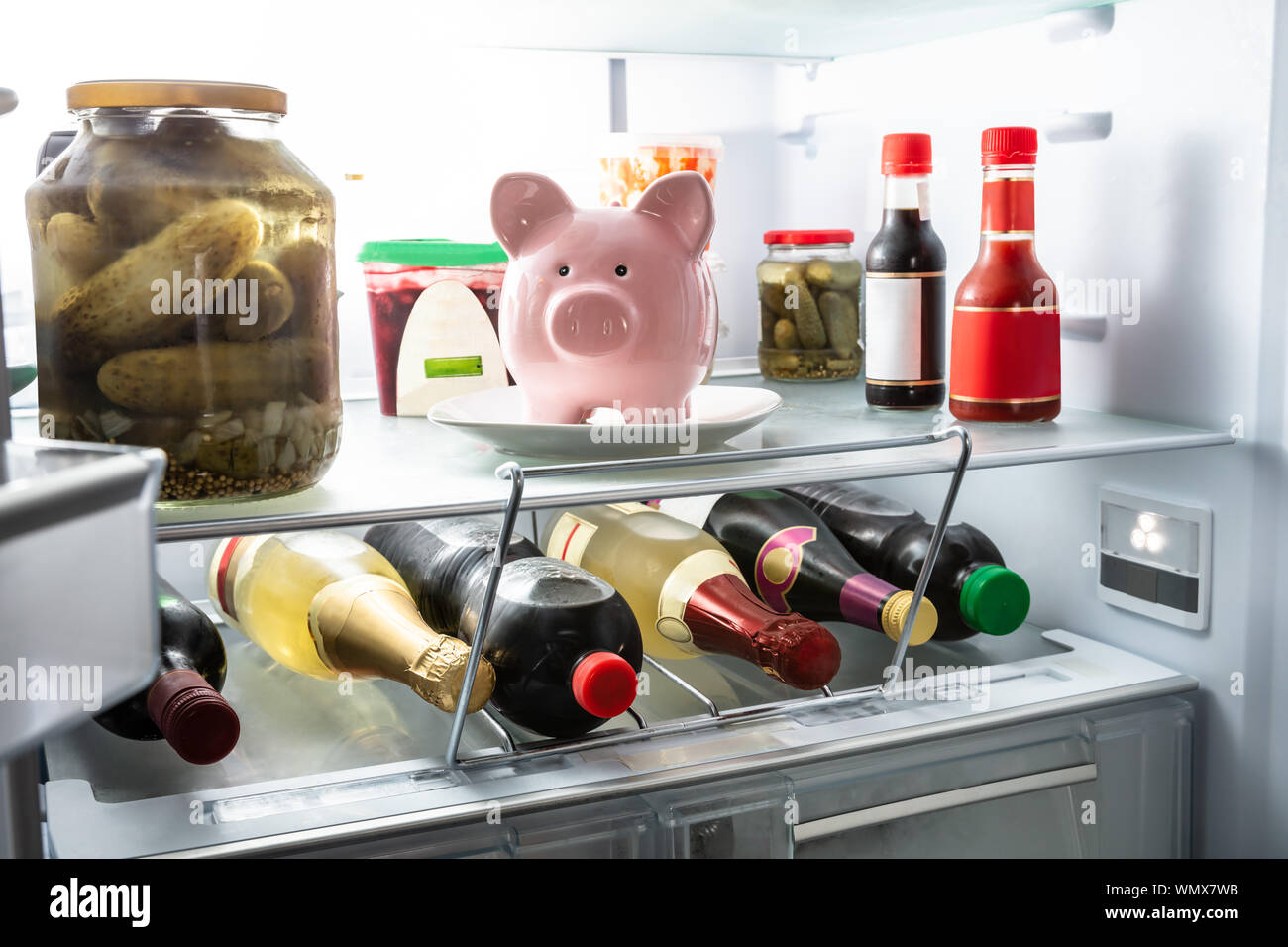 Pink Piggy Bank On White Plate Inside Refrigerator With Sauces And Preserved Food Stock Photo
