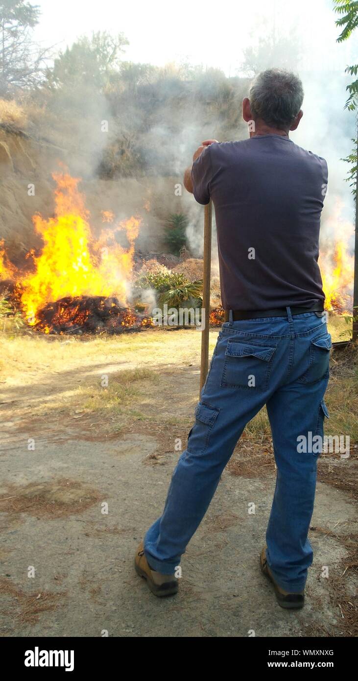 Rear View Of Man Standing By Fire On Field Stock Photo Alamy