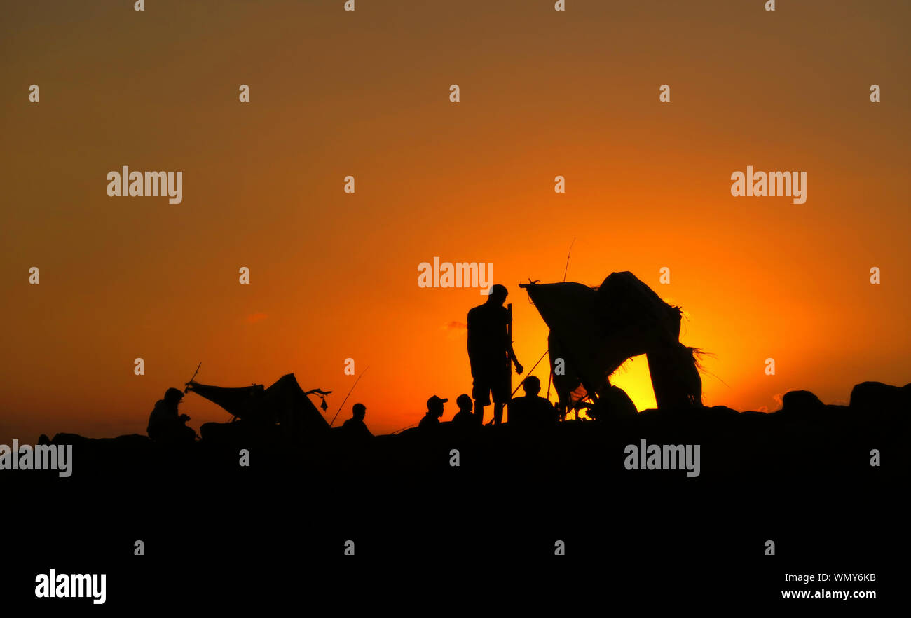 Silhouette Friends Camping On Field Against Sky During Sunset Stock Photo
