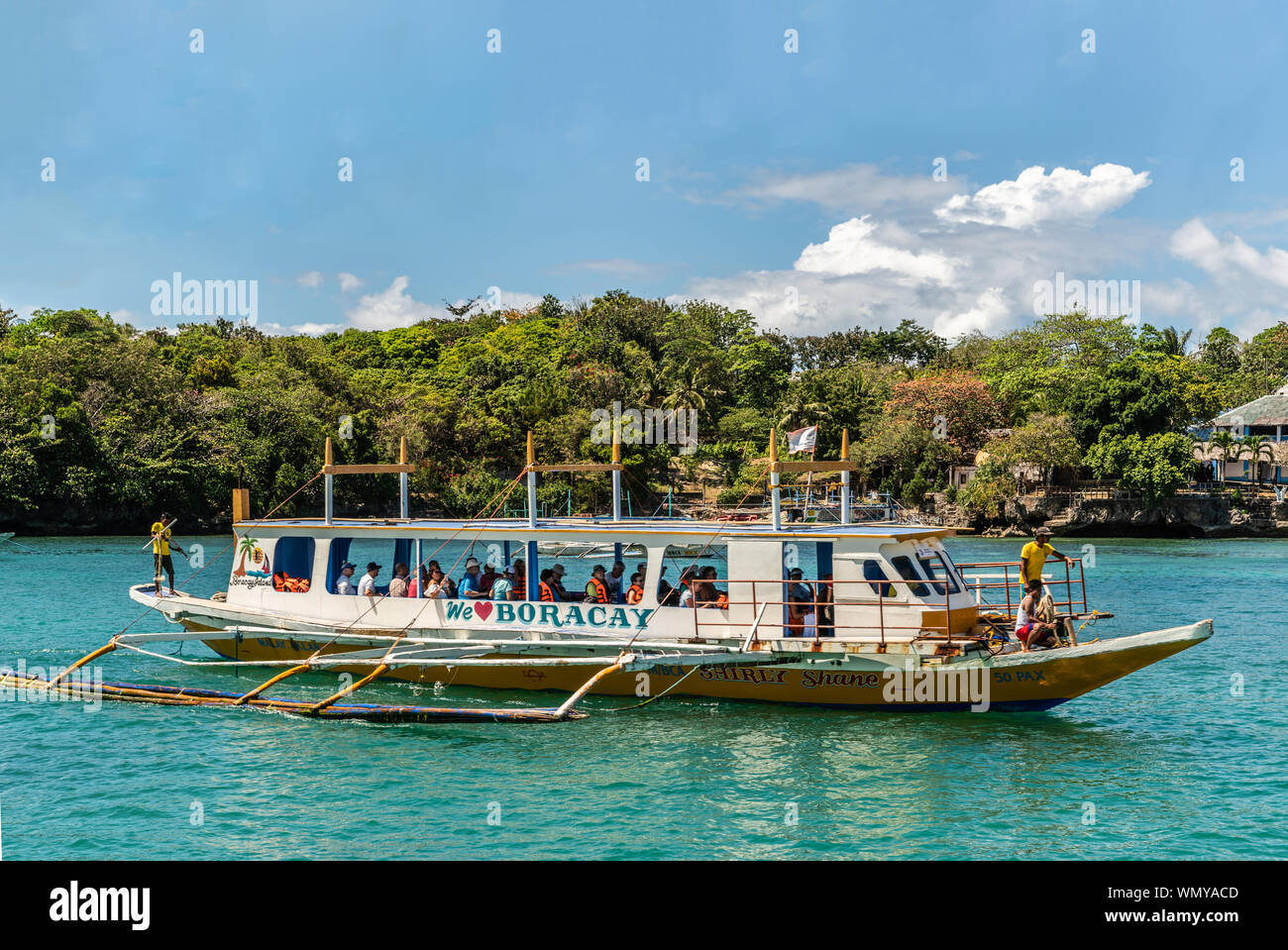 Manoc-Manoc, Boracay, Philippines - March 4, 2019: Closeup of white outrigger ferry on azure sea under blue sky with cloudscape and green tree band on Stock Photo