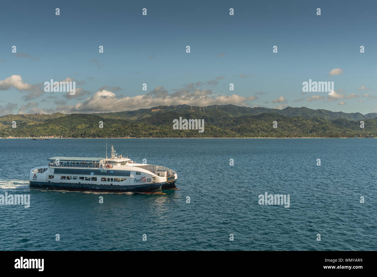 Manoc-Manoc, Boracay, Philippines - March 4, 2019: White and blue Fast Cat motorized modern long distance ferry sails on sea under blue sky. Mountains Stock Photo