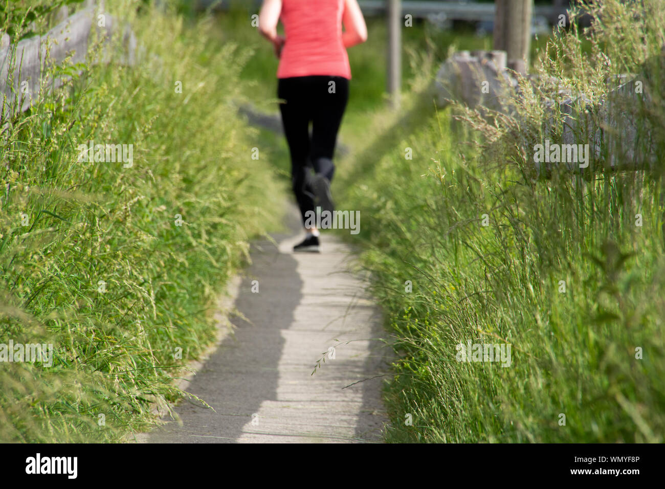 Fit woman runs along path in black leggings and pink top Stock Photo