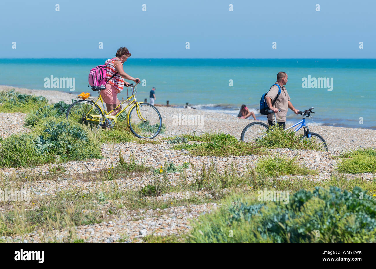 A couple arriving at a beach on bicycles on a hot June 2017 day in Summer in Littlehampton, West Sussex, England, UK. Stock Photo