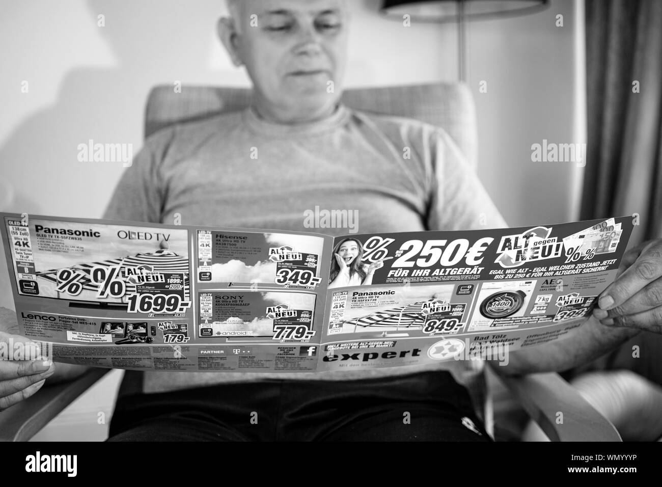 Paris, France - May 22, 2019: Senior man reading wide flyer advertising featuring on the cover multiple household products offered by Expert Oehler - 4k TV sets , washing machines Stock Photo