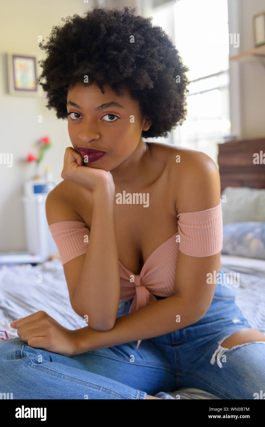 Young woman wearing off shoulder top sitting on  bed Stock Photo