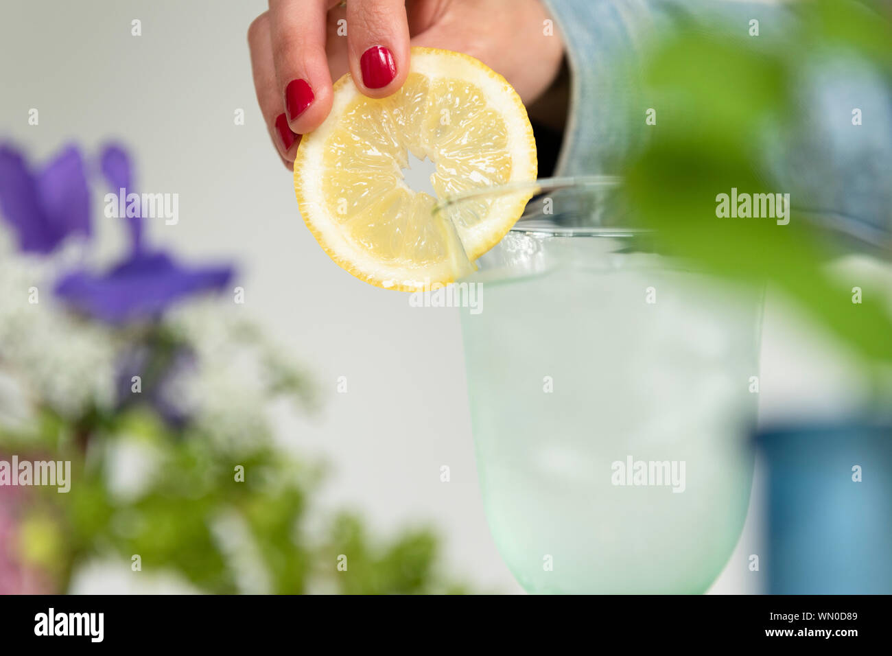 Woman putting lemon slice on glass of water Stock Photo