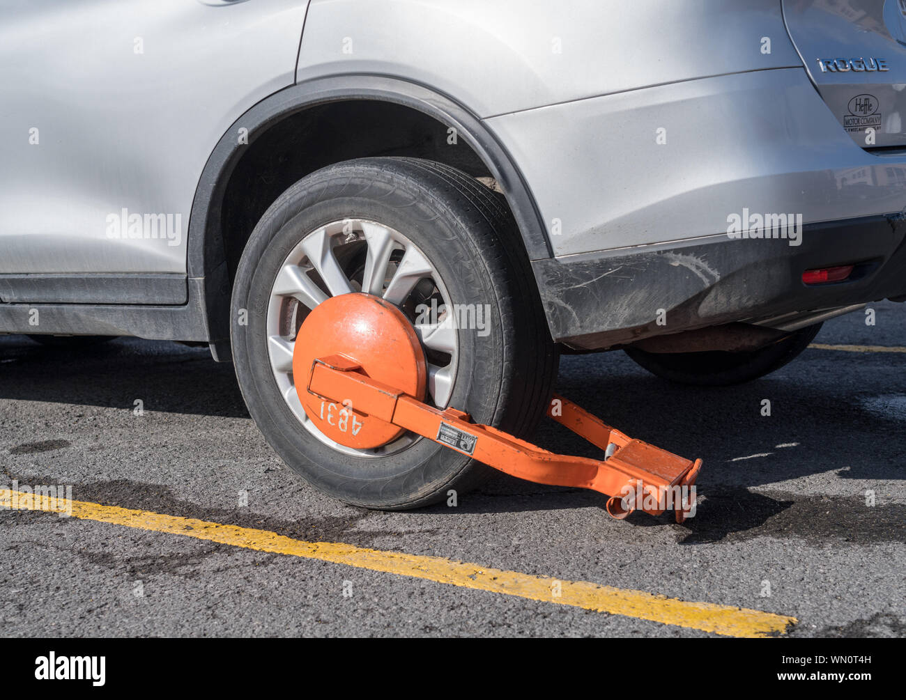 Parked car immobilized with orange parking clamp or boot Stock Photo