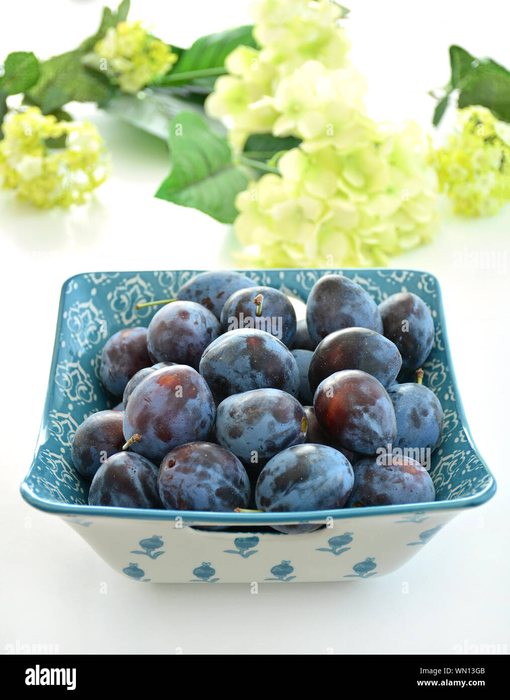 Fresh picked organic prune plums in decorative bowl on white background in vertical format.  Selective focus. Healthy food concept. Stock Photo