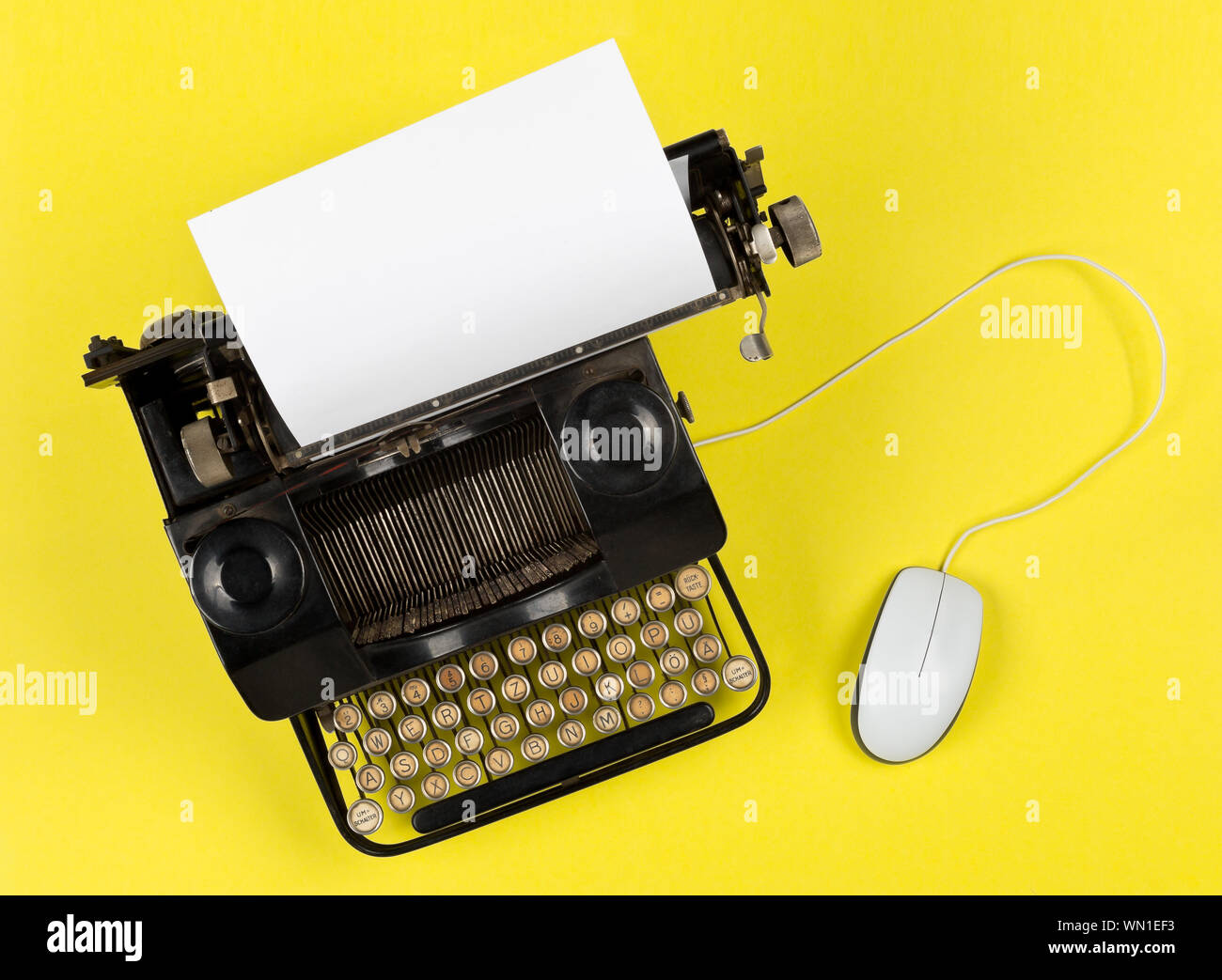 Antique retro mechanical typewriter with modern computer mouse on bright yellow background - digitalization, digitization or modernization minimal con Stock Photo