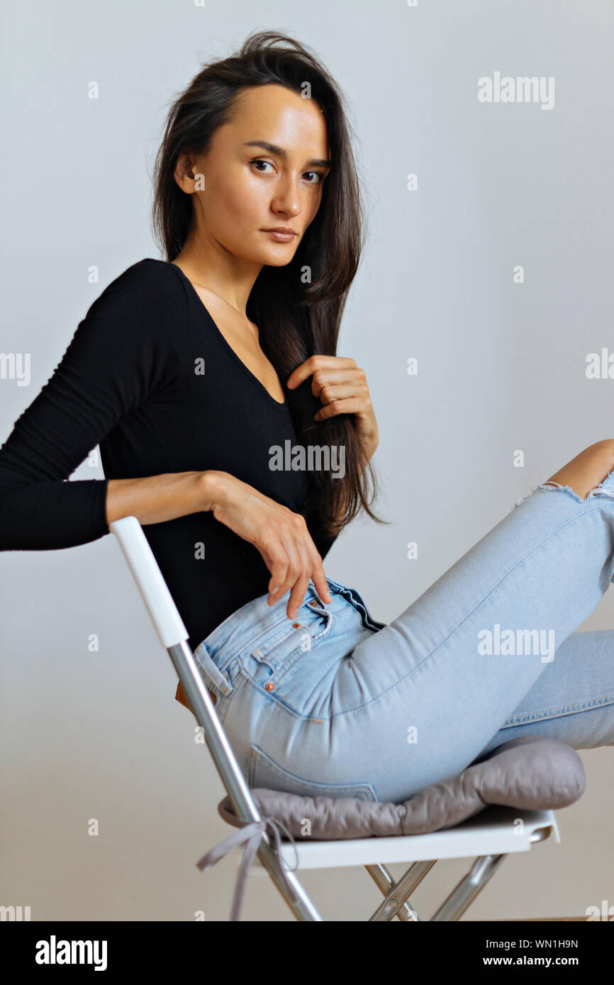 Woman wearing black top and ripped jeans on chair Stock Photo - Alamy
