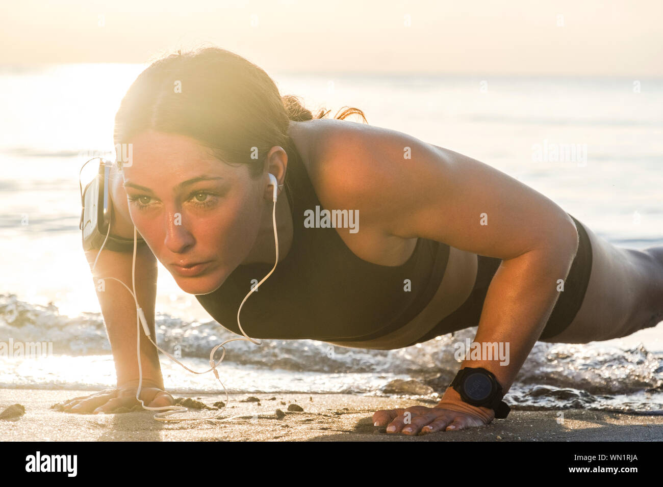 Woman wearing headphones doing push-up on beach Stock Photo