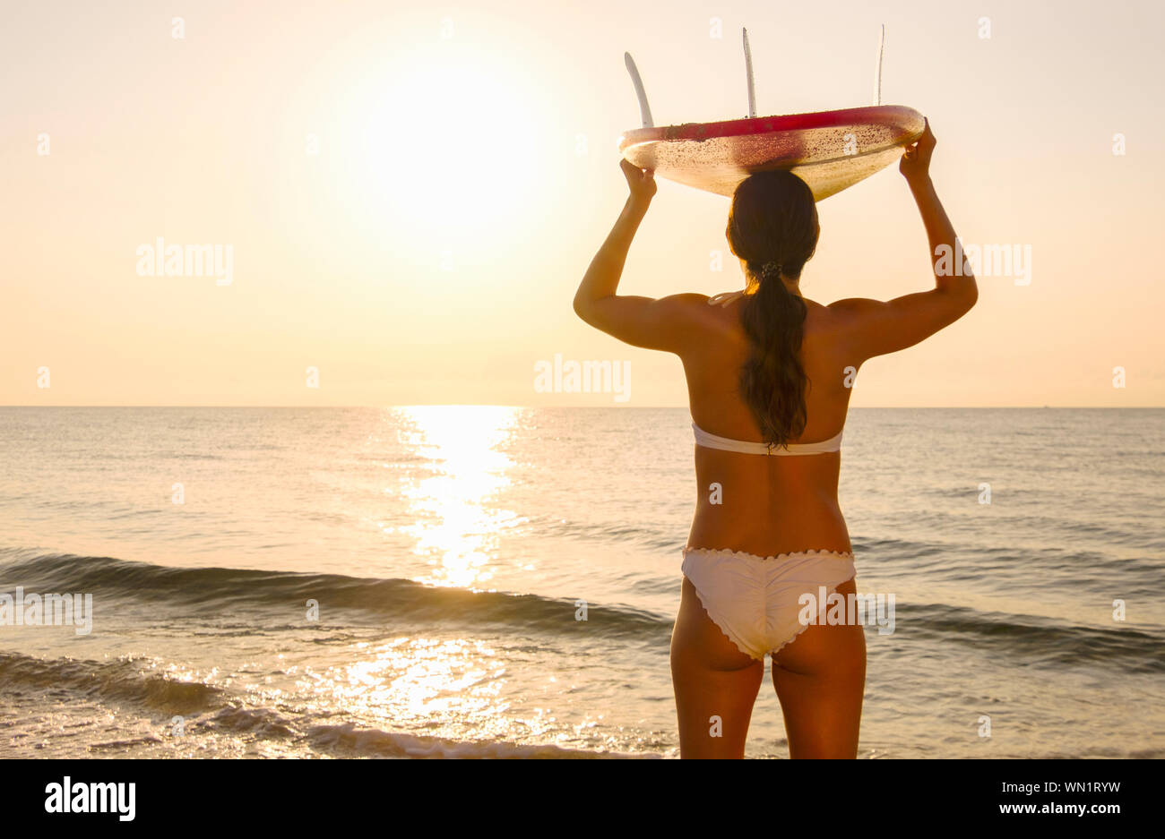 Woman with surfboard on her head on beach at sunset Stock Photo