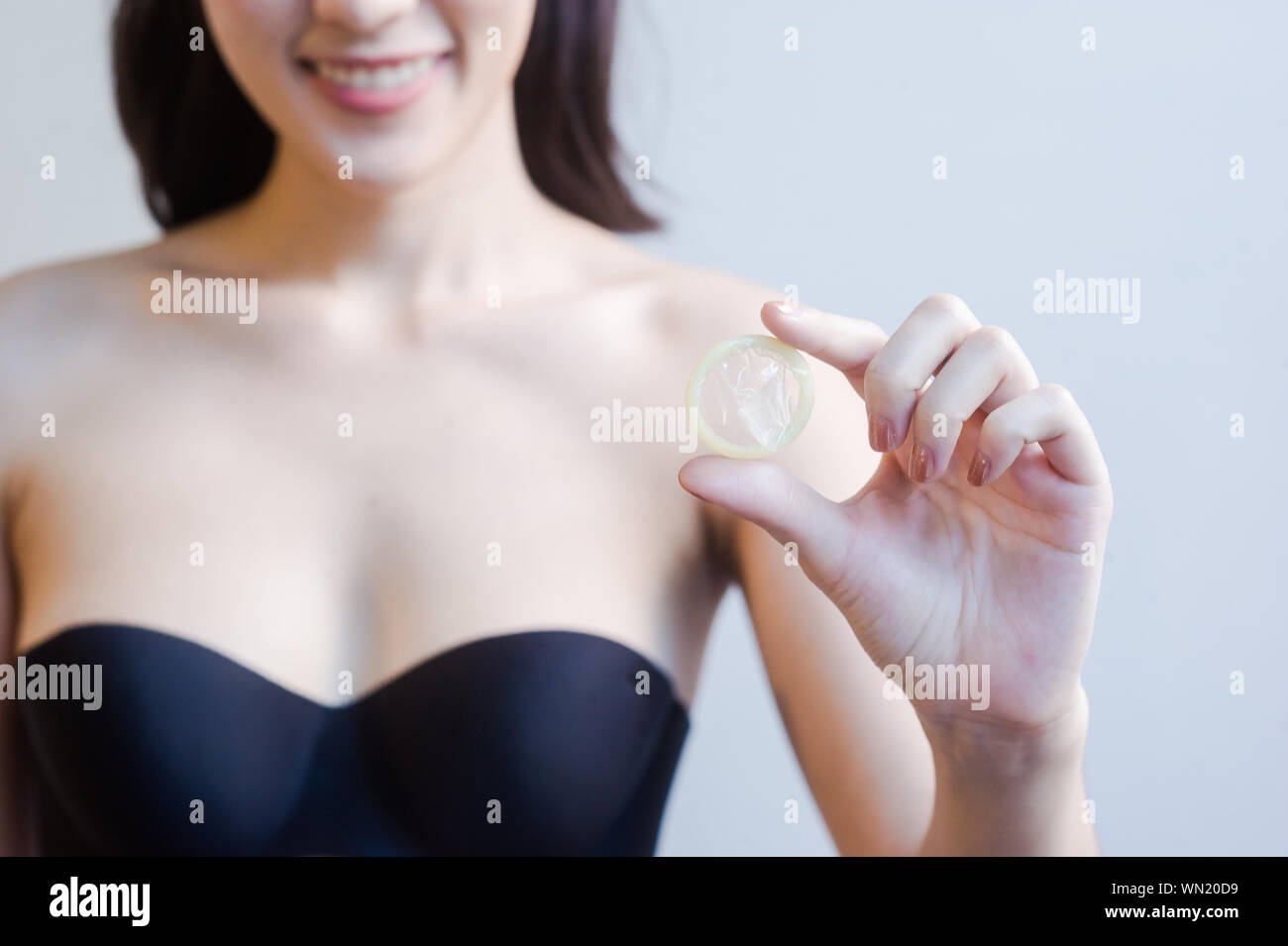 Midsection Of Smiling Young Woman Holding Condom Against White Background Stock Photo