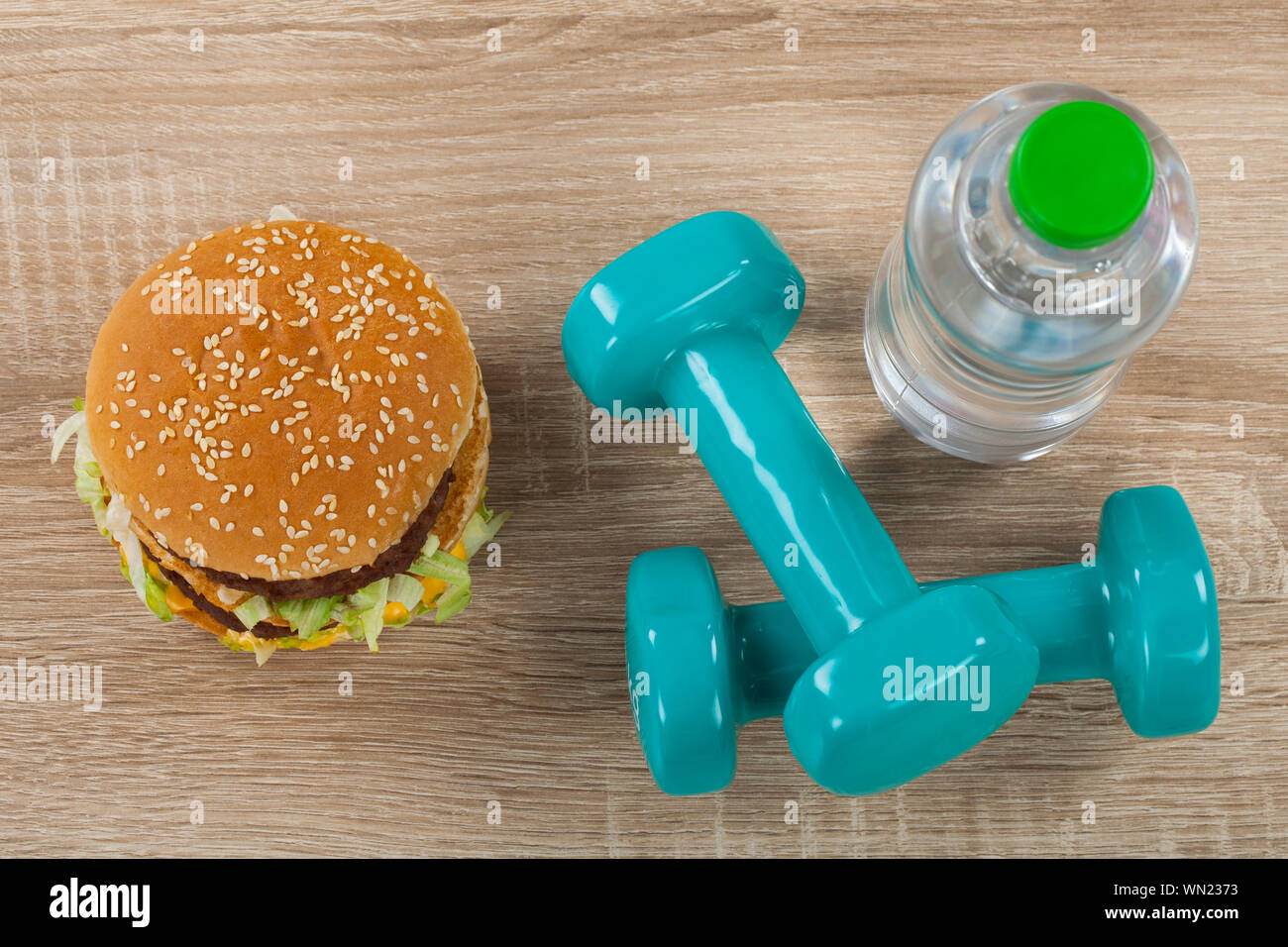 Top view of juicy cheeseburger, still water and blue dumbbells diet