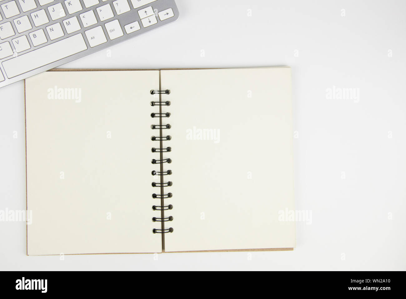 Directly Above Shot Of Spiral Notebook By Computer Keyboard On White Background Stock Photo