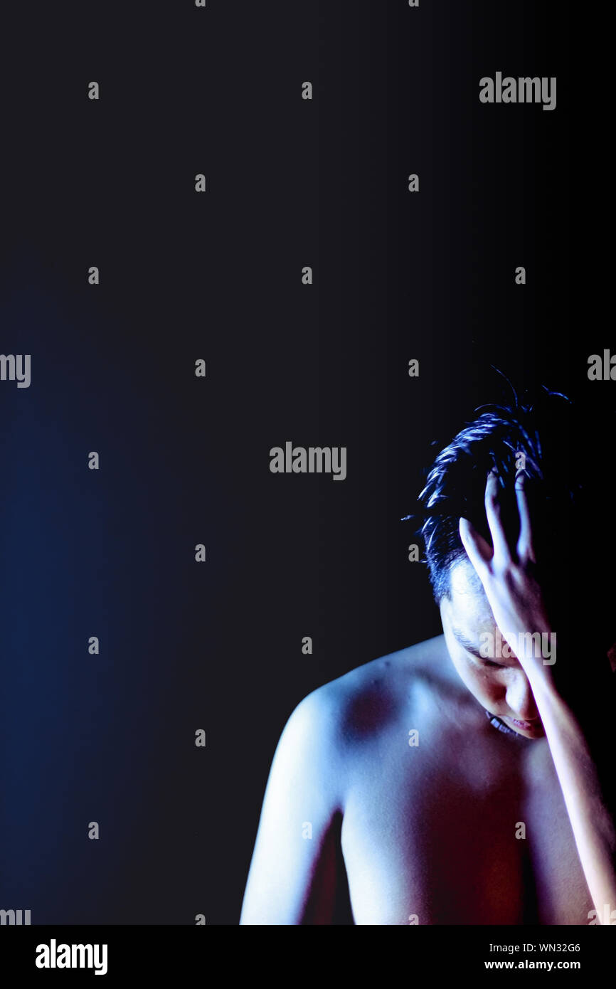 Young Man With Hand In Hair Standing Against Black Background Stock Photo