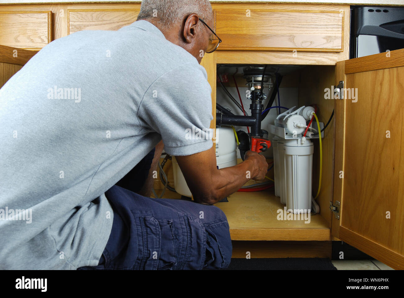 Mature Man With Wrench Tighten Pipes Under Sink At Home Stock Photo