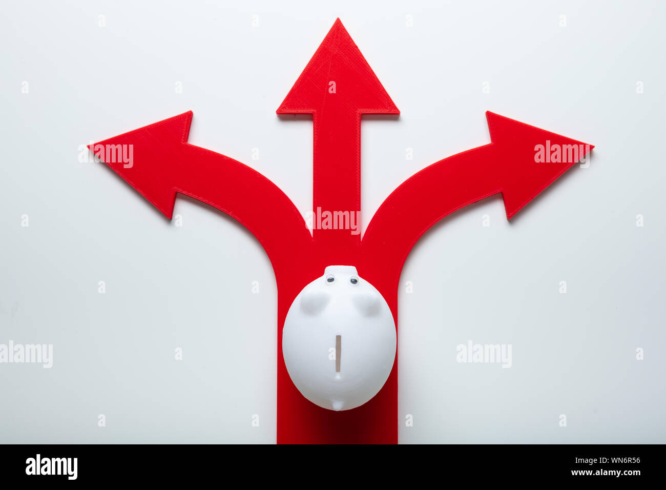 Elevated View Of Piggybank Over Red Arrow Signs Showing Various Direction Against Isolated Stock Photo