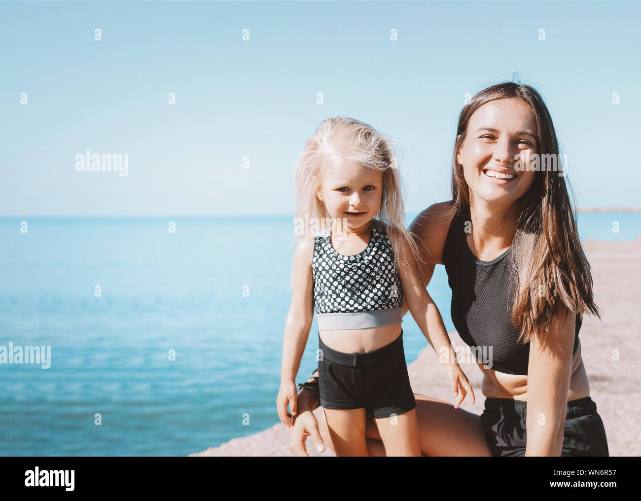 Young fit woman mom with little cute girl exercising on sea beach together, healthy lifestyle Stock Photo