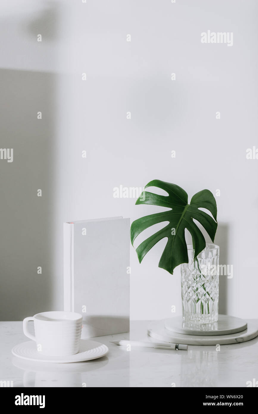 Monstera tropical palm leaves in a glass vase standing on office table ...