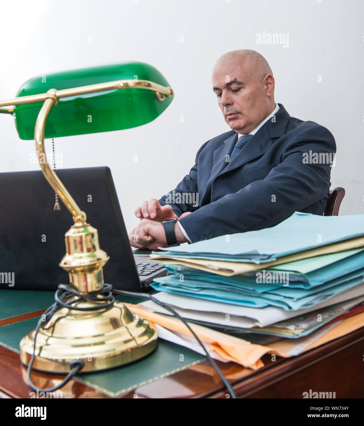 Businessman Looking At Wrist Watch While Sitting In Office Stock Photo