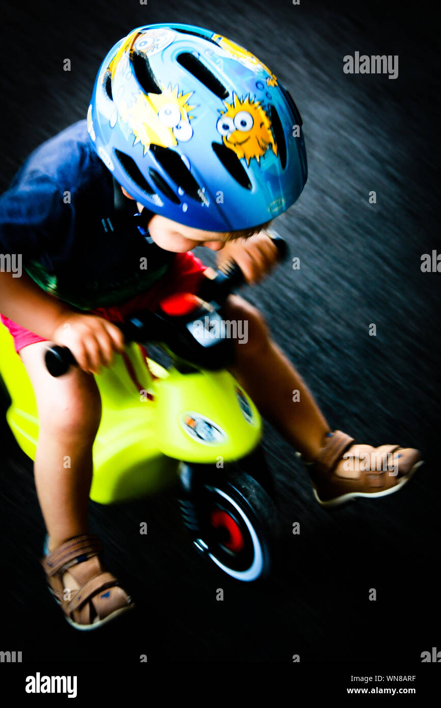 2 years old boy driving his toy moped with high speed across his playground Stock Photo