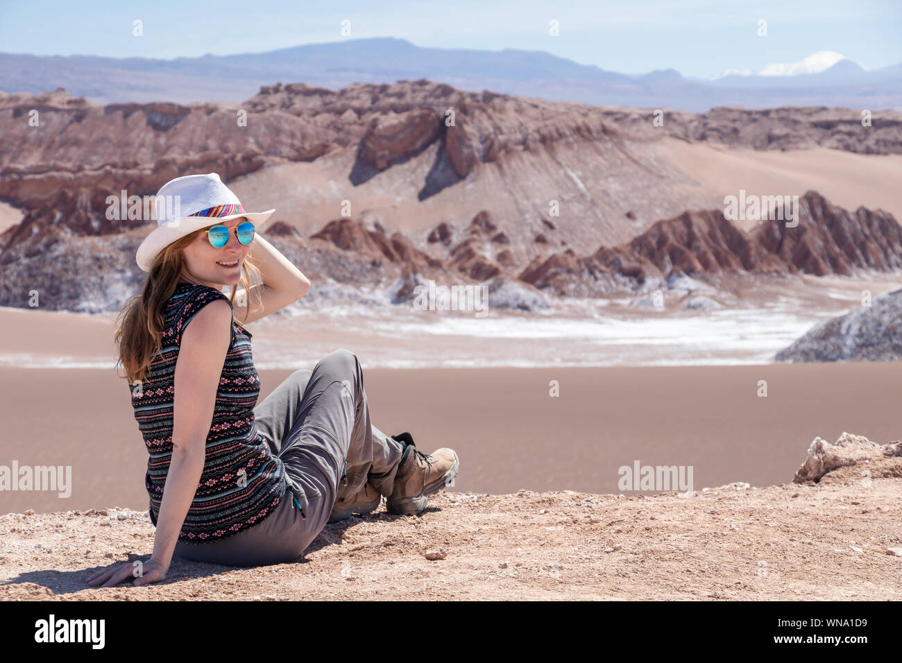 Young blond caucasian woman alone sitting and admiring untouched nature of Moon Valley in Atacama desert, Chile. Outstanding landscape background with Stock Photo