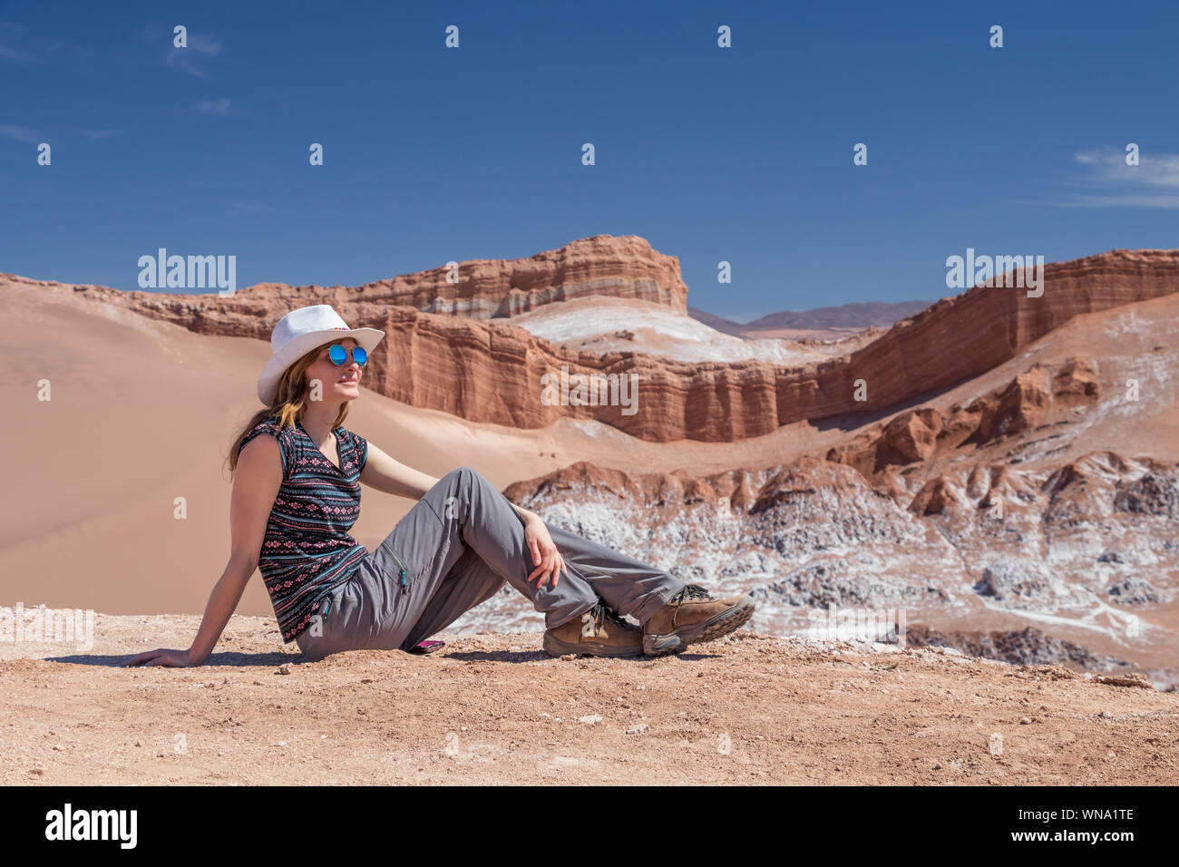 Young blond caucasian woman alone sitting and admiring untouched nature of Moon Valley in Atacama desert, Chile. Outstanding landscape background with Stock Photo