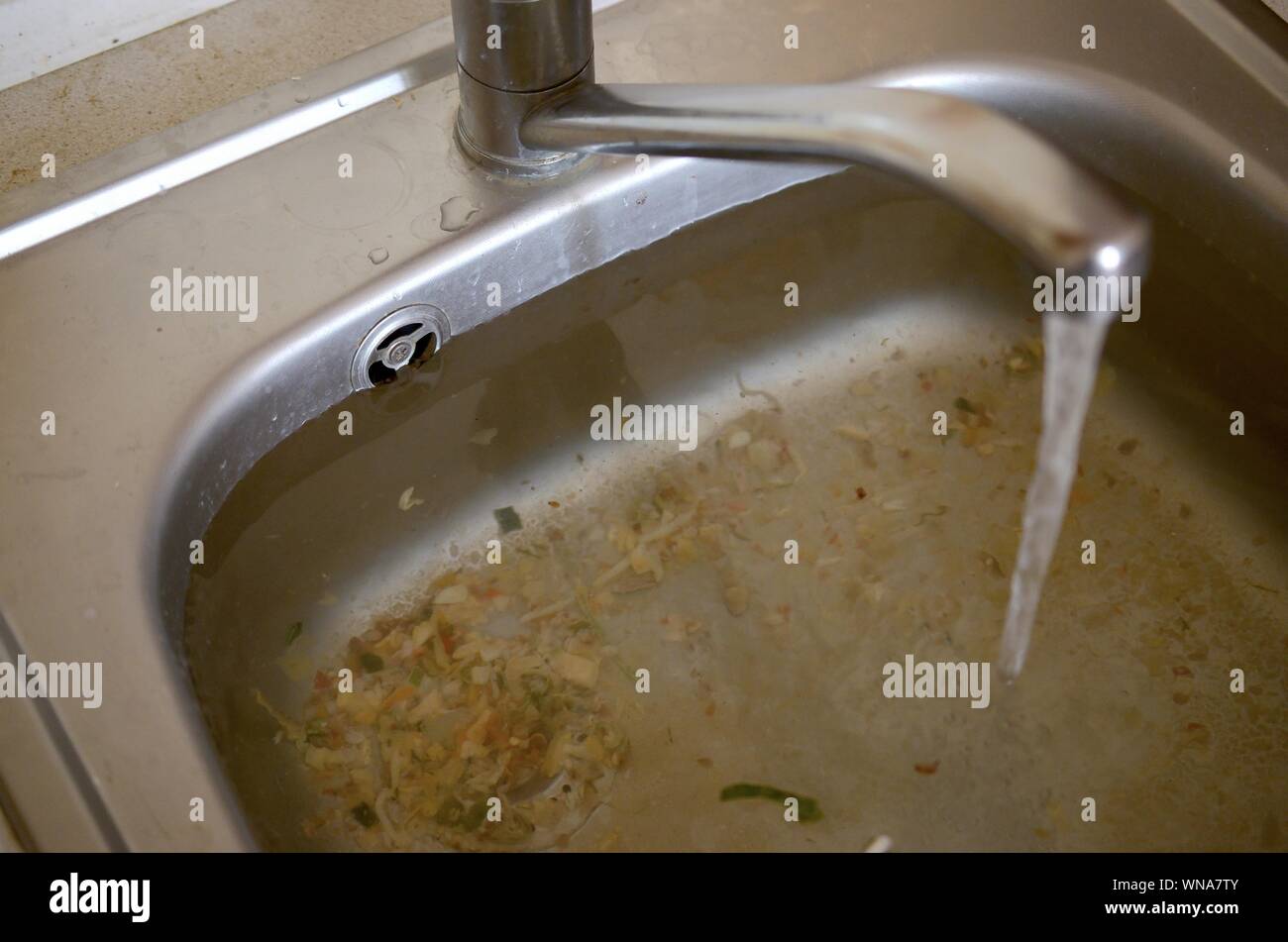 Stainless steel sink plug hole close up full of water and particles of food. Overflowing kitchen sink, clogged drain. Problems with the water supply Stock Photo