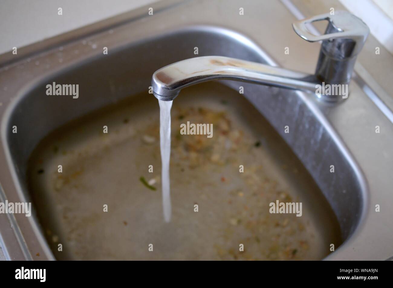 Stainless steel sink plug hole close up full of water and particles of food. Overflowing kitchen
