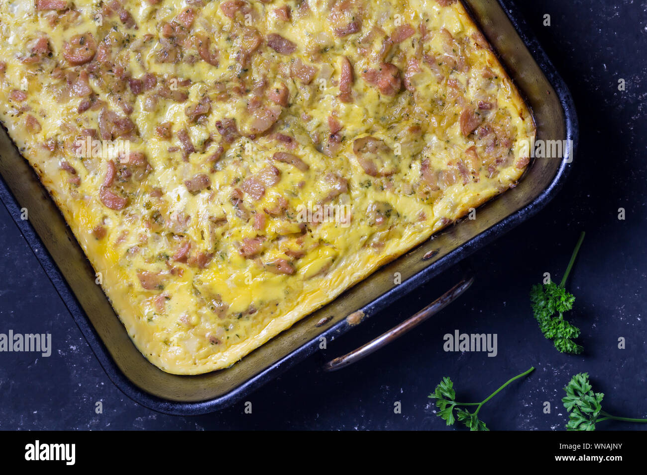 Cheesy bacon and sausage breakfast bake in oven tray on black