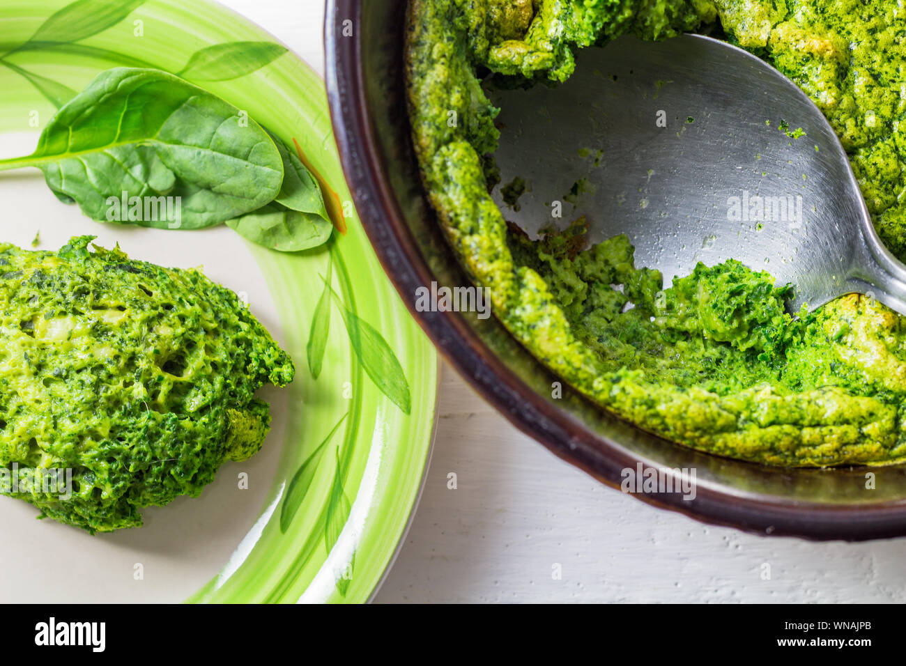 Baked spinach souffle in souffle dish with serving spoon and creamy