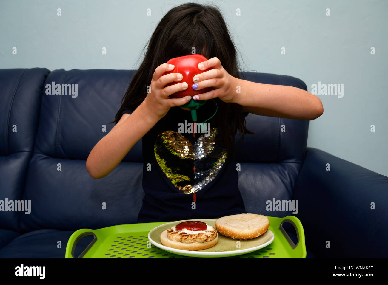 Young girl squirting tomato ketchup on a chicken burger Stock Photo