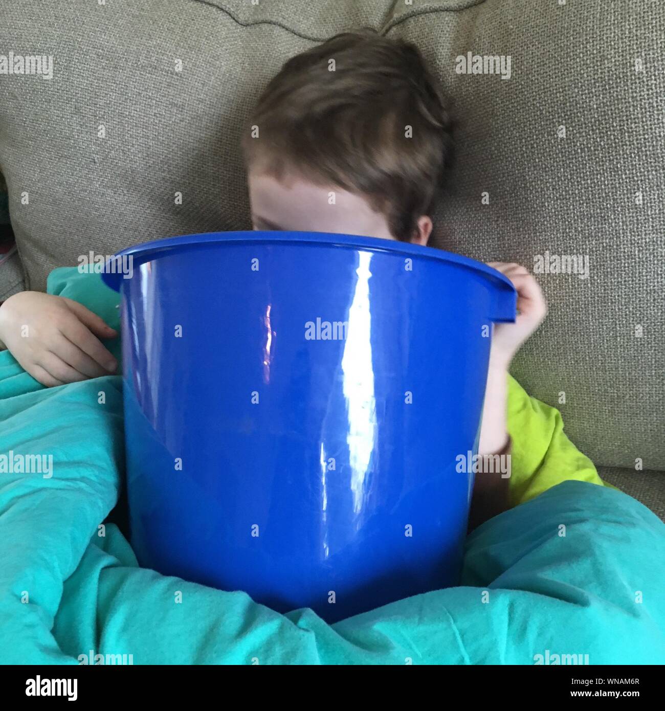 Sick Boy Vomiting In Bucket While Lying On Bed Stock Photo