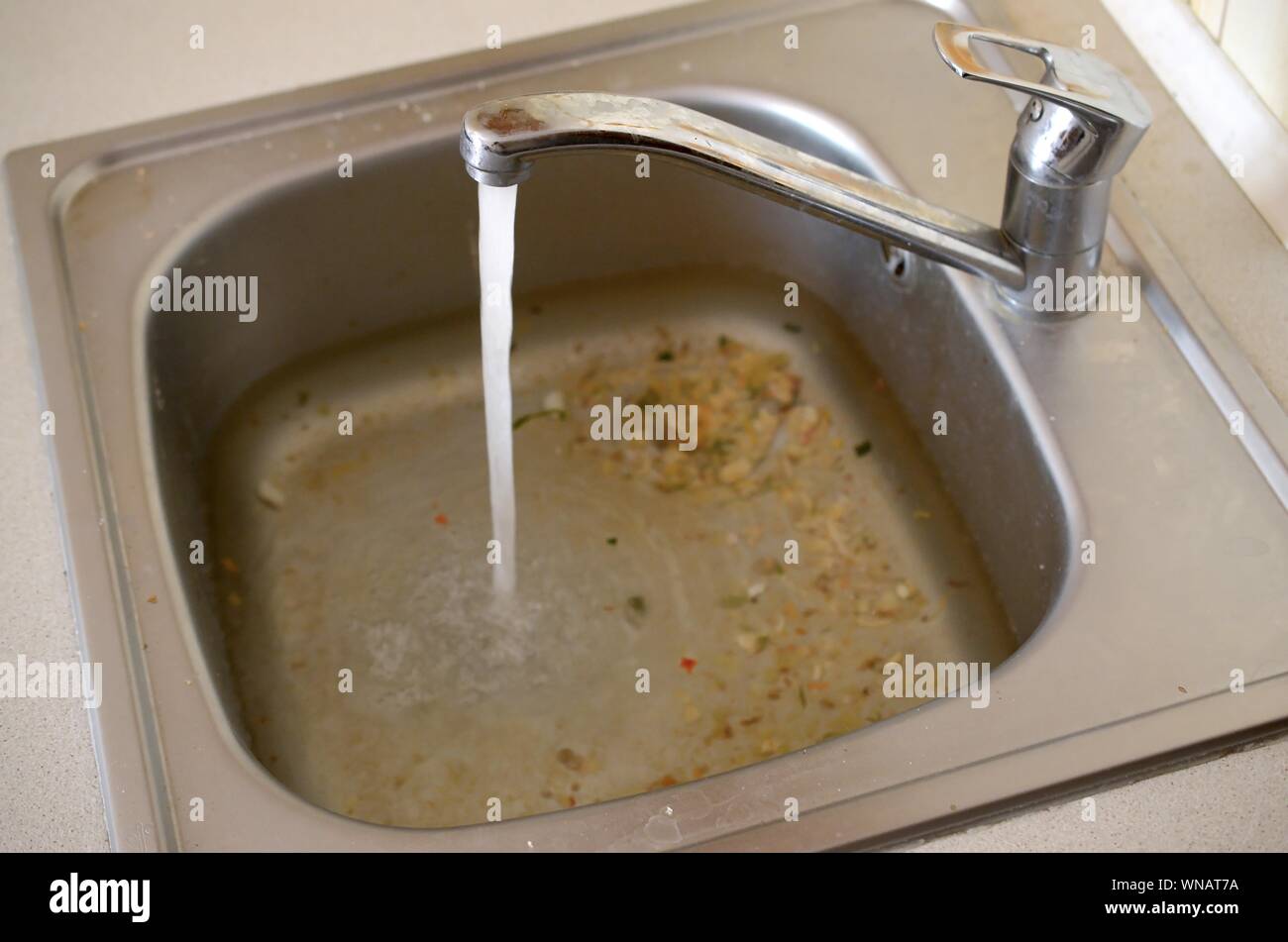 Stainless steel sink plug hole close up full of water and particles of food. Overflowing kitchen