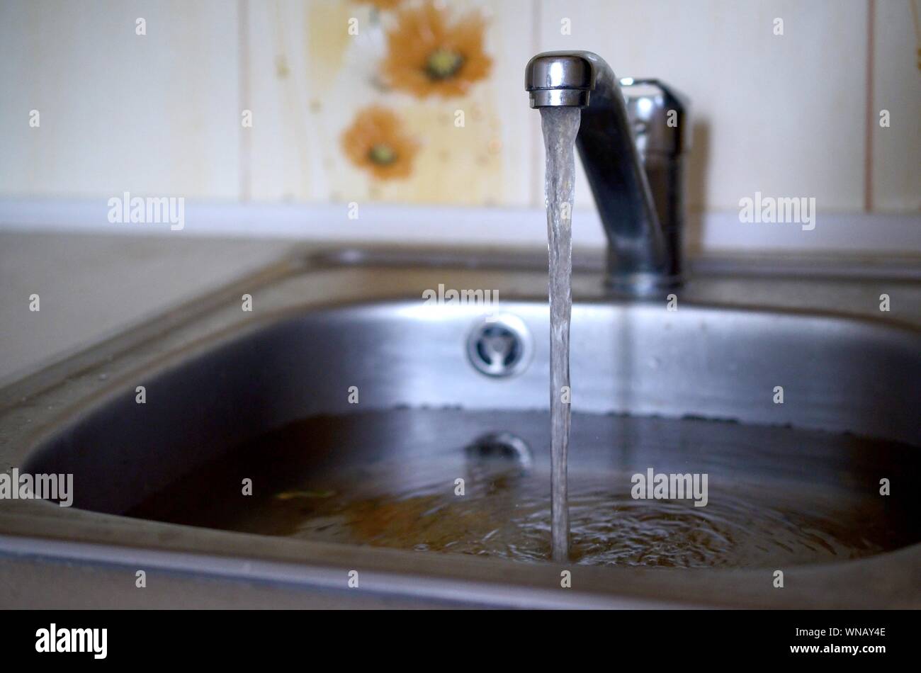 Stainless steel sink plug hole close up full of water and particles of food. Overflowing kitchen sink, clogged drain. Problems with the water supply Stock Photo