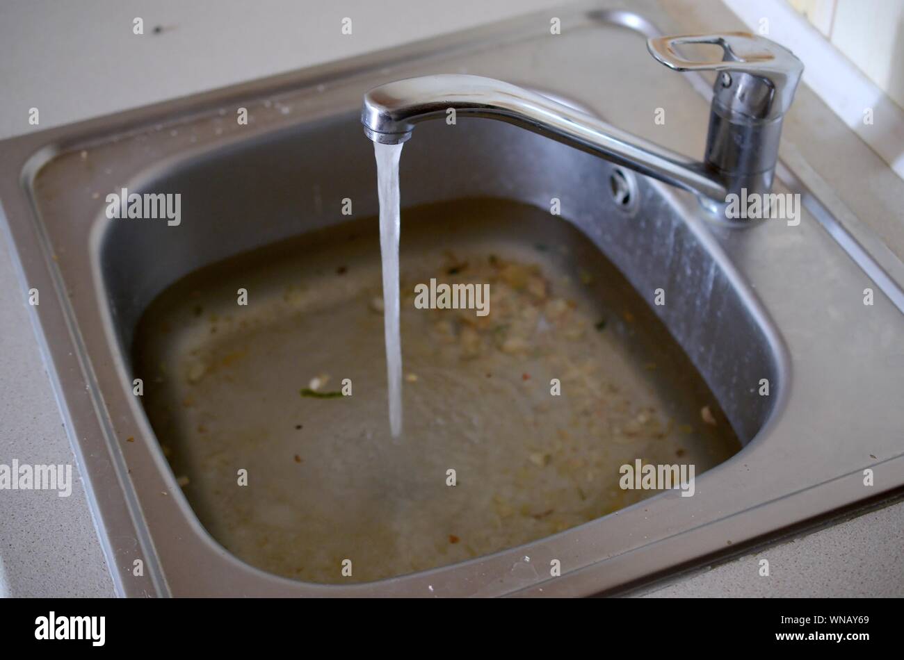 Stainless steel sink plug hole close up full of water and particles of food. Overflowing kitchen