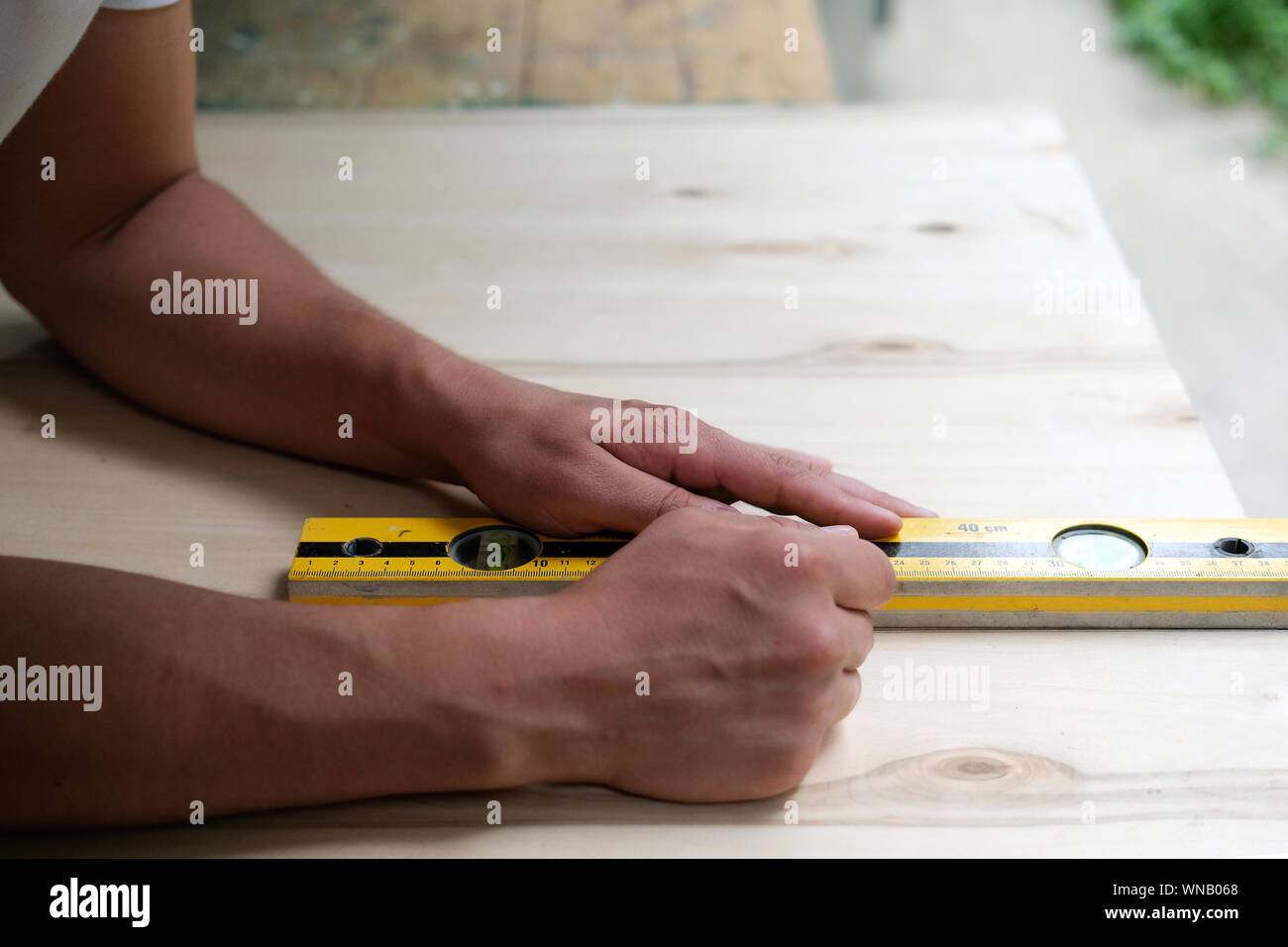 Carpenter marking straight line on plywood sheet using spirit level in