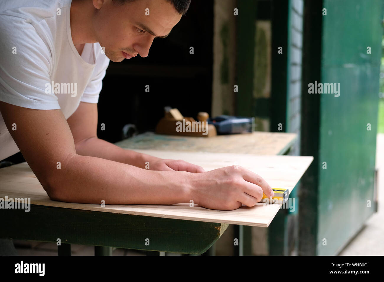 Carpenter marking straight line on plywood sheet using spirit level in