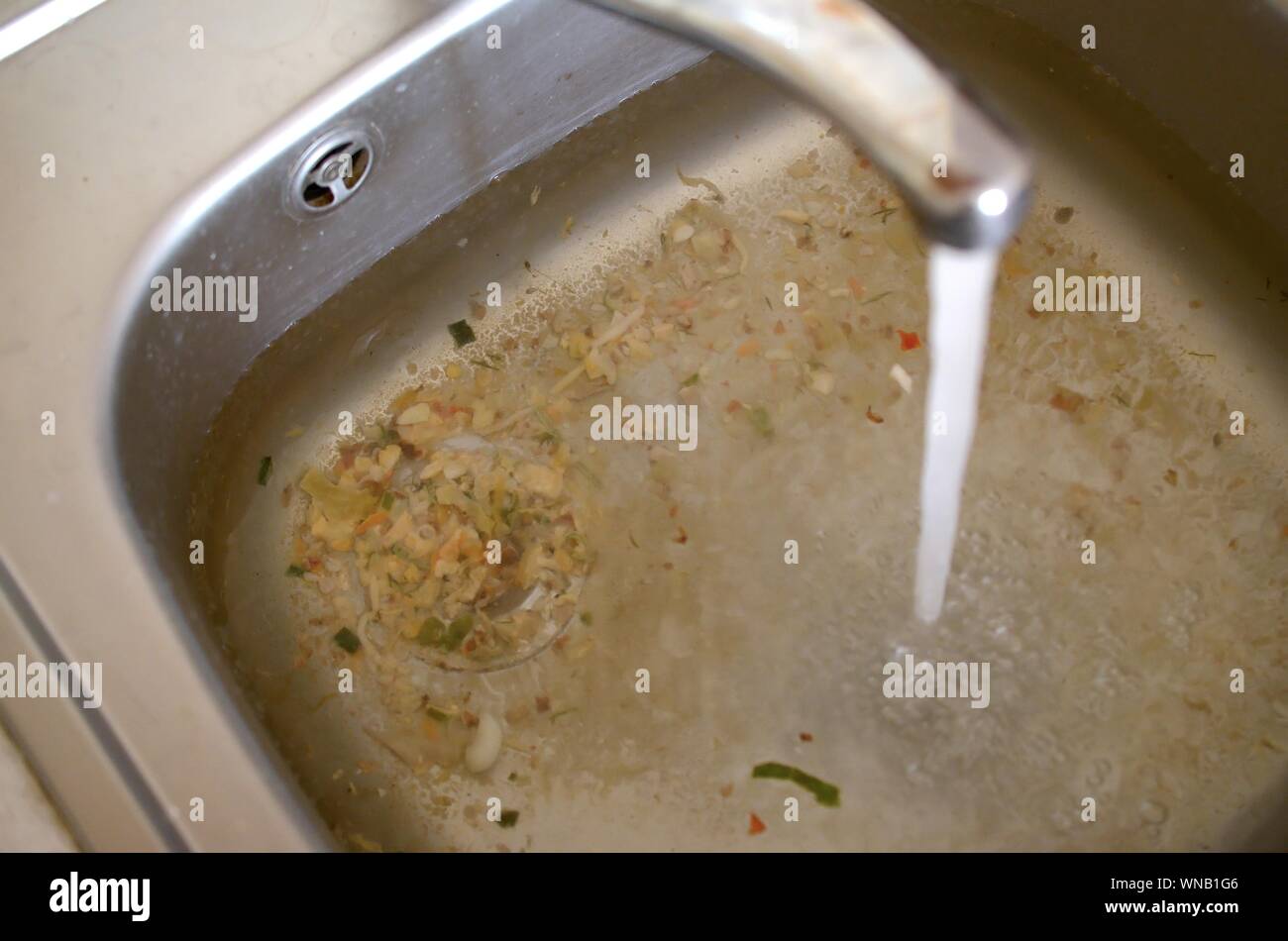 Stainless steel sink plug hole close up full of water and particles of