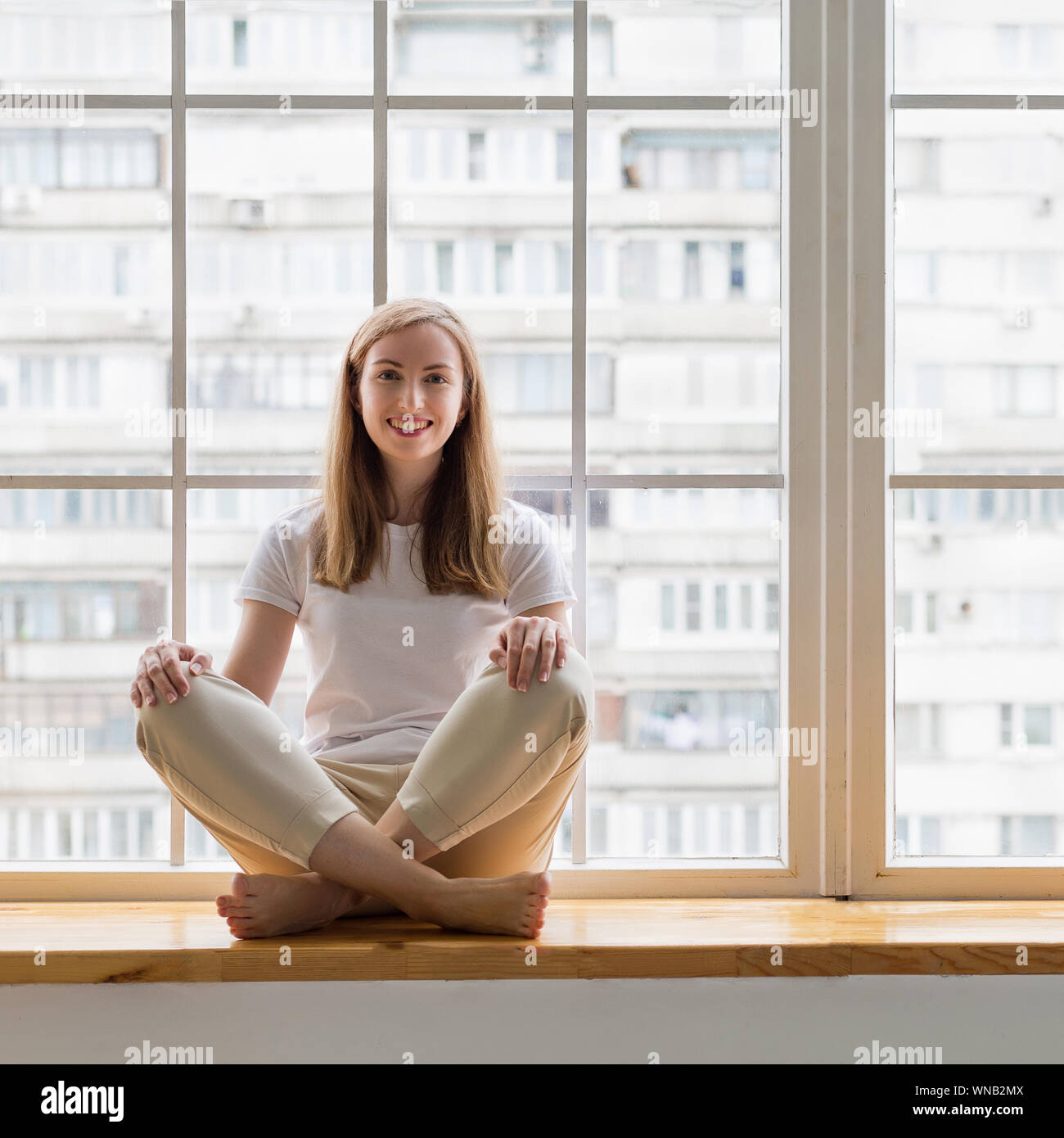 Young smiling woman sitting on window sill Stock Photo