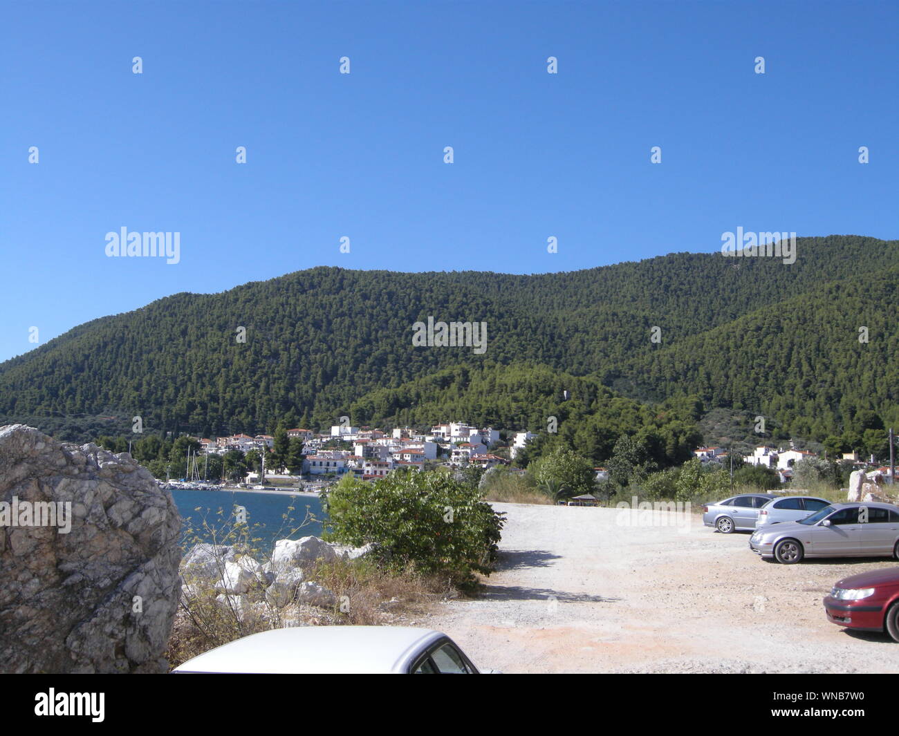 Cars Parked In Lot Next To Sea With Hills In Background Stock Photo