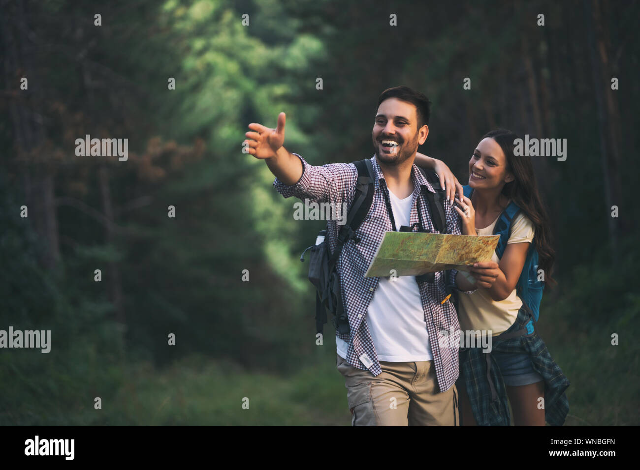 Happy couple is hiking in forest. They are looking at map Stock Photo ...