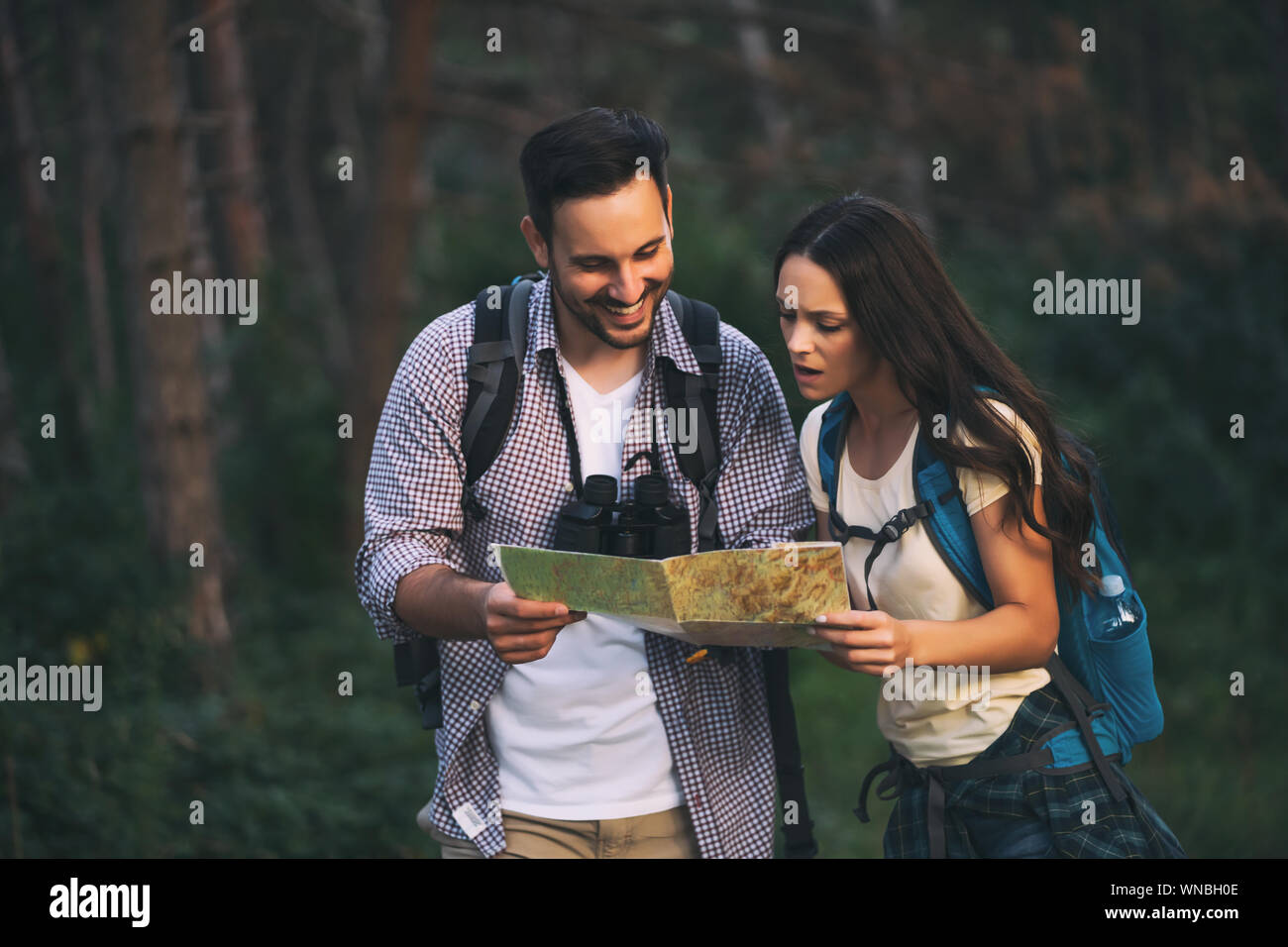 Happy couple is hiking in forest. They are looking at map Stock Photo ...