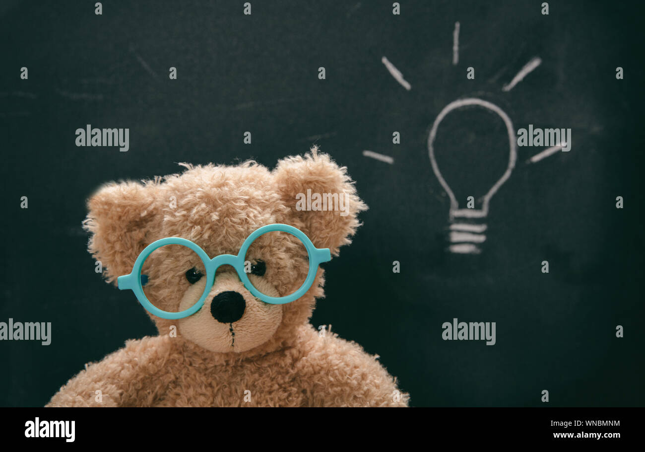 Bright idea, solution. Smart kid cute teddy wearing blue eyeglasses in class, lightbulb sketch on blackboard, Stock Photo