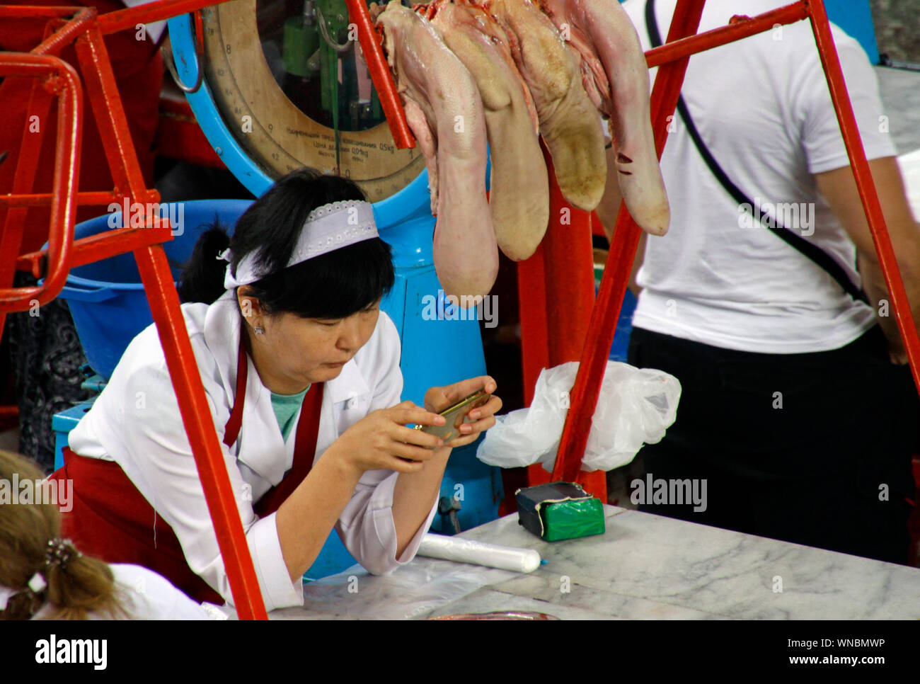 Almaty, Kazakhstan - August 22, 2019: Saleswoman under a row of cow tongues in the meat section of the famous Green Bazaar of Almaty, Kazakhstan. Stock Photo