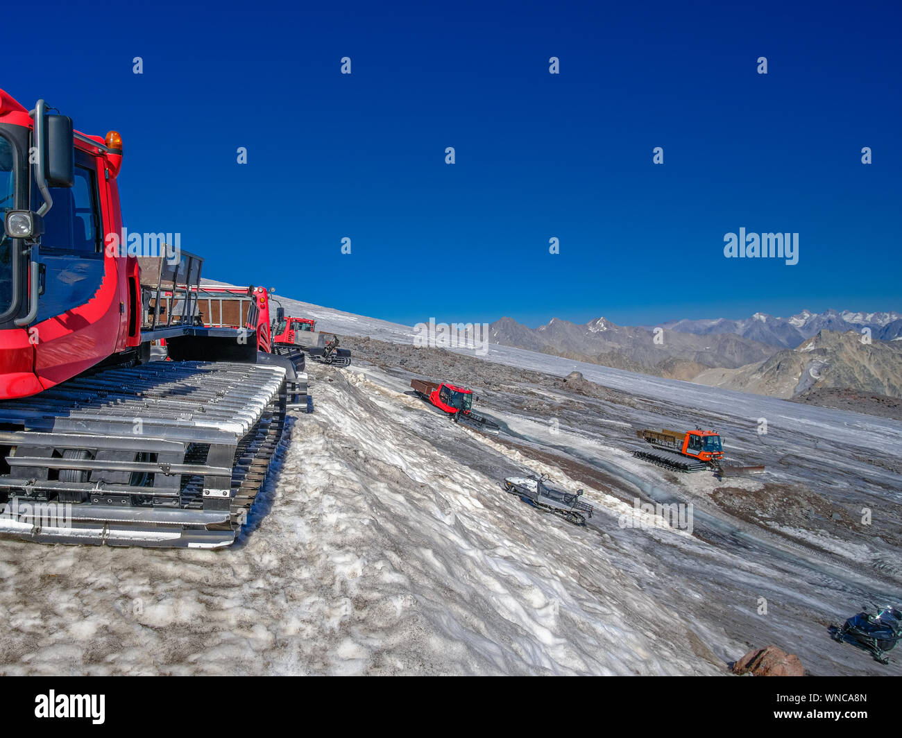 Special caterpillar equipment on the slope of Mount Elbrus against the backdrop of a mountain range. Blue cloudless sky and bright sunlight. Stock Photo