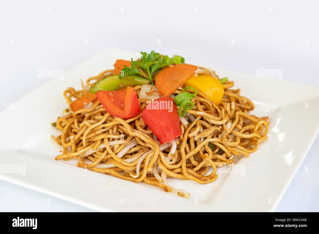 Chinese fried noodle server with fresh vegetable and on a square white plate Stock Photo